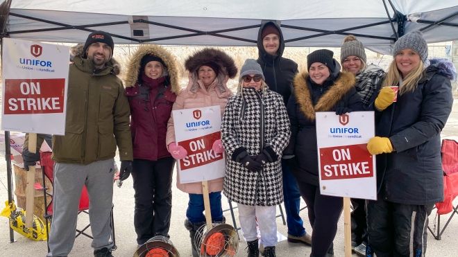 Eight Unifor members post outside in cold weather, three holding On Strike placards