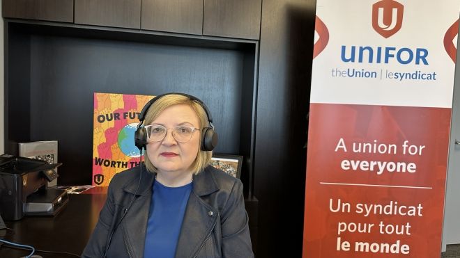 A women wearing headphones sits at a desk in font of a poster and pop up banner