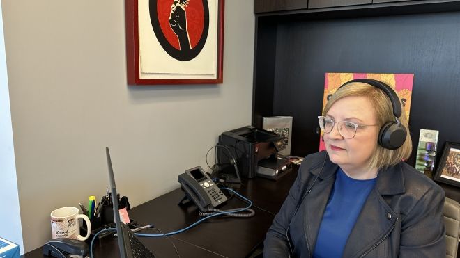 A women sits at a desk looking at a screen, wearing headphones