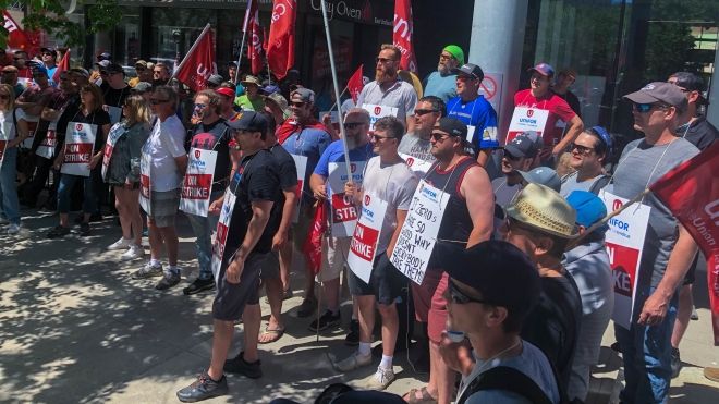 Large group of Unifor members with flags and On Strike signs outside at a rally in downtown Winnipeg