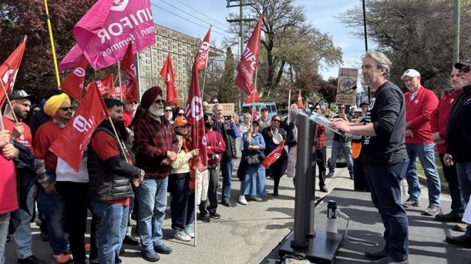 A man speaking at a podium to a crowd holding Unifor flags