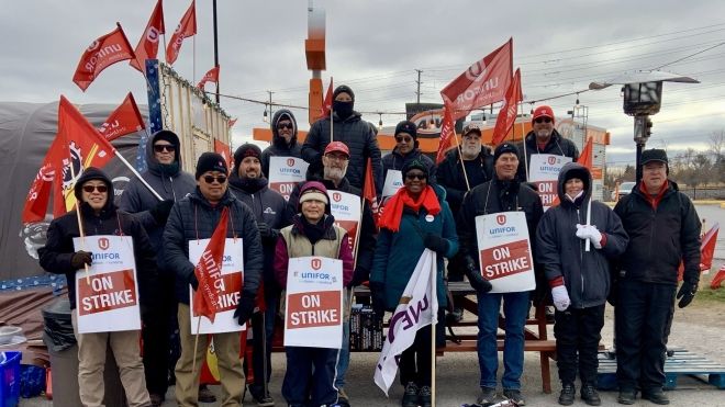 Fourteen people posing outside in warm cloths holding placecards and Unifor flags