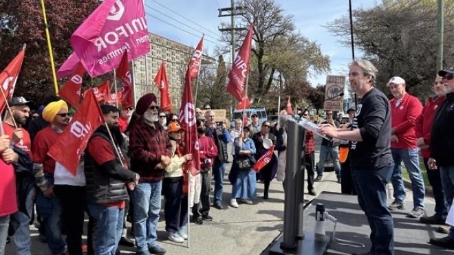 A man speaking at an outdoor rally at a podium to a crowd holding flags