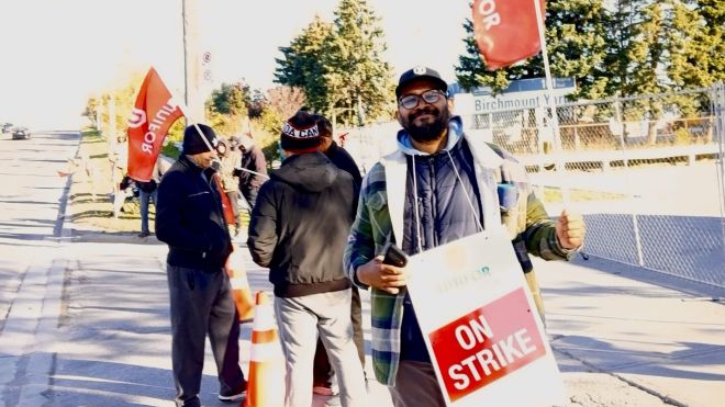 A man holding a "ON Strike" placcard and a red Unifor flag