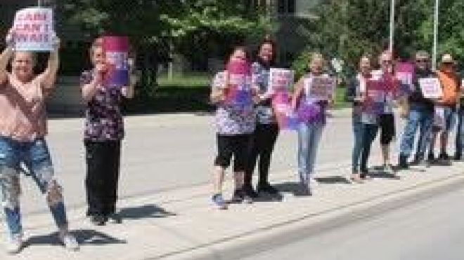 Health care workers holding picket signs standing out front of a long term care home