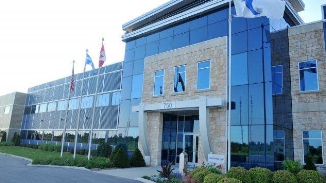 Building with glass and brick and four flags out front, with manicured hedges.
