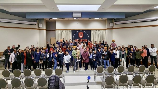 large group gathered for a photo at the front of a union hall with a Unifor logo centre stage.