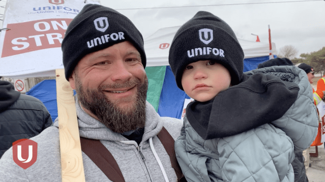 Close up of father and toddler, both wearing black and white Unifor toques.