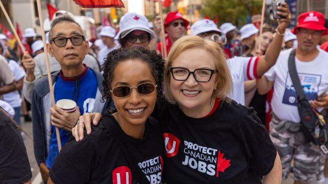 Two women embracing in front of a huge crowd marching in the Labour Day parade