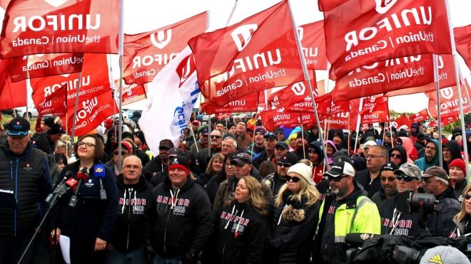 Rally at Coop Refinery during their 2019 lockout. Large crowd holds Unifor flags and stands behind Lana Payne