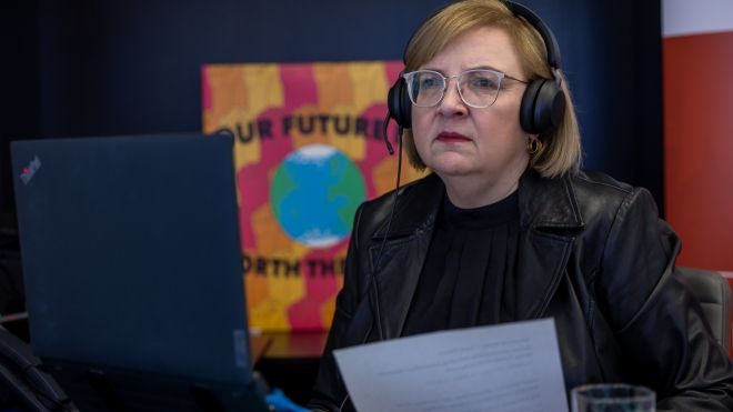 A woman wearing a headset holds a paper and stares at computer screen.