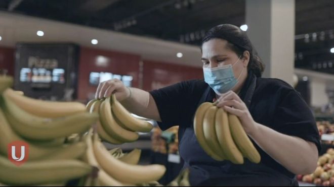 A grocery store worker wearing a mask sorts bananas.