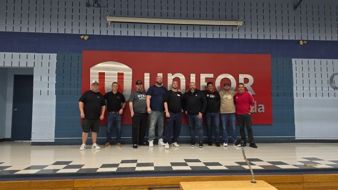 A group of men posing in front of a Unifor sign