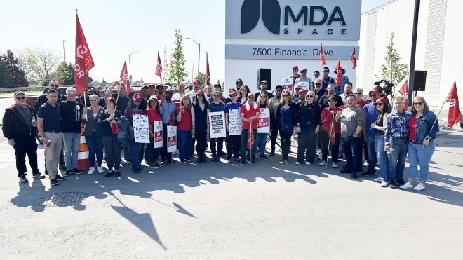 A group of people standing holding up flags outside in front of an MDA Space exterior sign