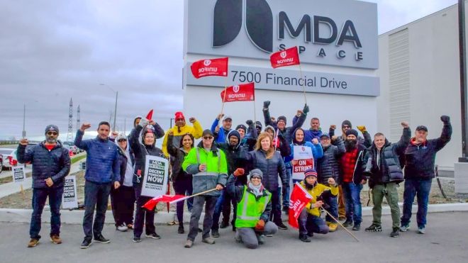 Workers with raised fists stand in front of the MDA Space headquarters in Brampton, Ontario