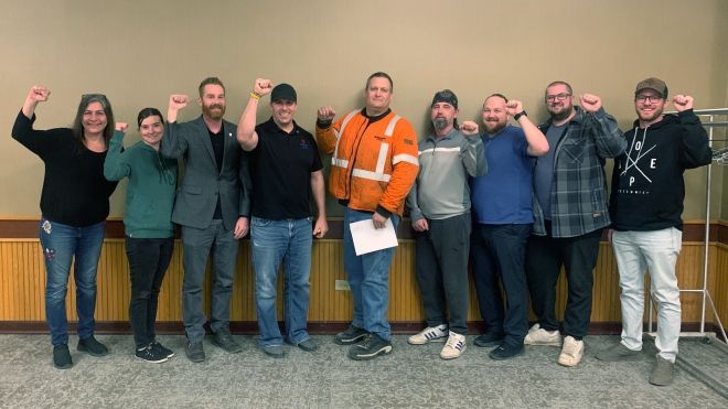 Nine people standing for a photo indoors with their fists raised in the air.