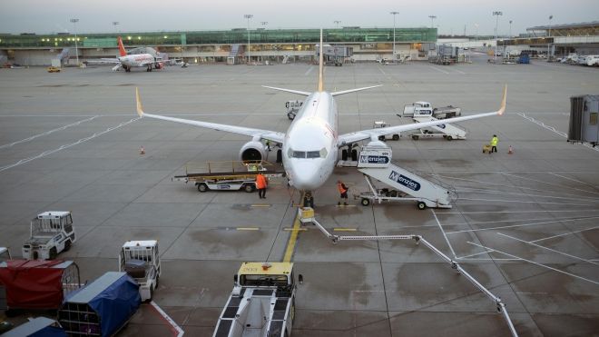 An airplane on the tarmac, surrounded by several workers and stairs with “Menzies” on the side.