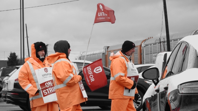 Striking workers carry flags and signs on a picket line.