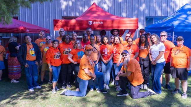 A large group in orange shirts pose outside in front of tents.
