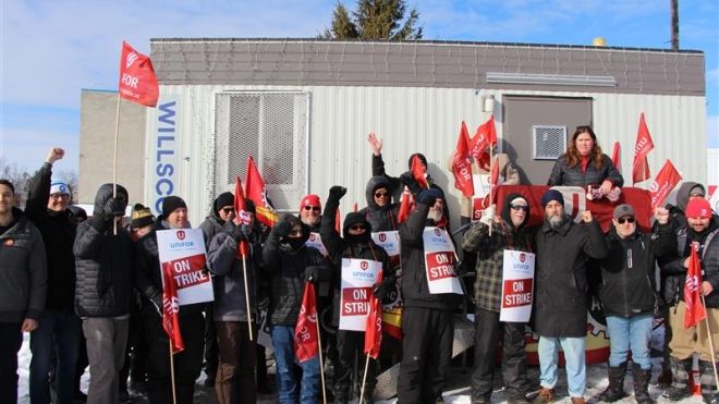 A large group holding Unifor flags and placard that read "on strike"