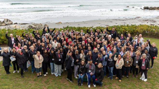 Large group of Unifor members posing outdoors beside a rocky beach, many raising their fists, with ocean waves in the background.
