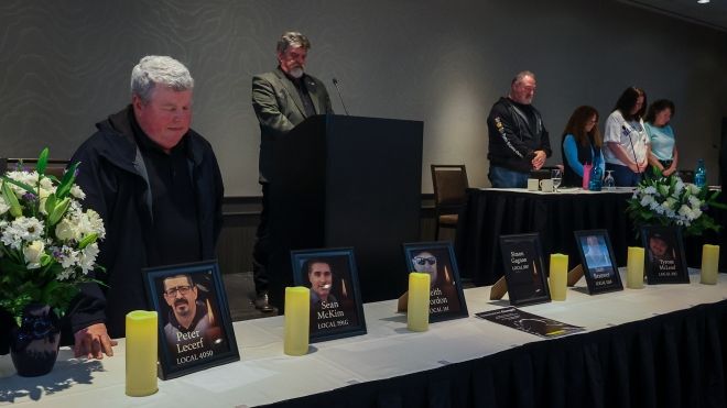 six people with their heads bowed stand behind a table with candles and portriats 