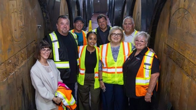 Eight people standing in between rows of large wine barrels