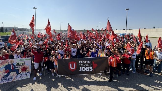 A large rally of poeple standing behind a banner holding flags