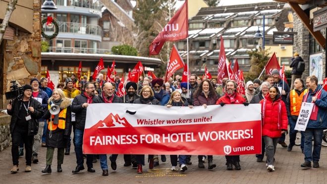 Group of people holding a banner saying "Fairness for hotel workers" others holding flags