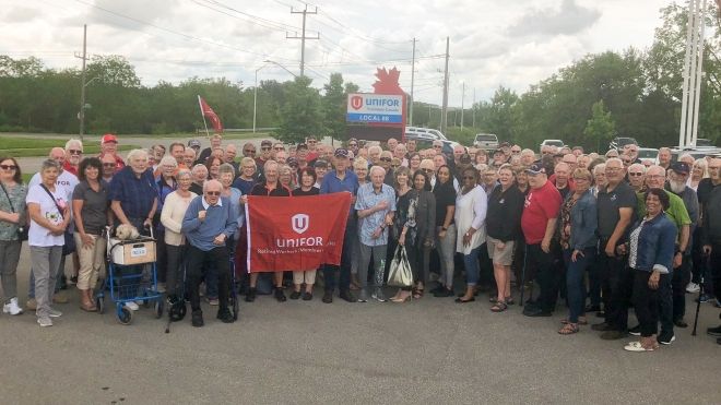 A large group of retirees standing posing for a photo in front of a Unifor Local 88 exterior sign