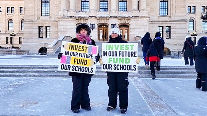 Two people outside the Sask Legislature Building holding hand-made signs reading 'Invest in our future, fund our schools