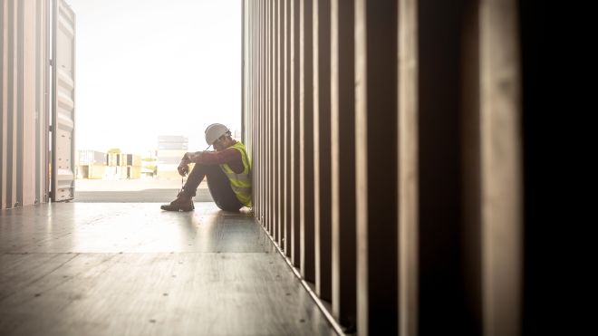 Sad worker sitting with head down and arms wrapped around knees