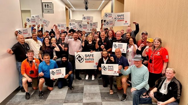 A group of people raising their fists in solidarity, holding Safe Rates campaign signs.