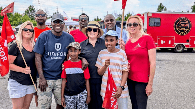 A group of people posing outdoors at a rally holding flags a food truck in the background
