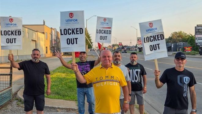 Six men stand on a sidewalk holding signs that read "UNIFOR LOCKED OUT," indicating a labor dispute.
