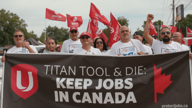 Unifor members and supporters hold a large banner reading “Titan Tool & Die: Keep Jobs in Canada” while raising fists and standing in front of a sea of red Unifor flags at a rally.