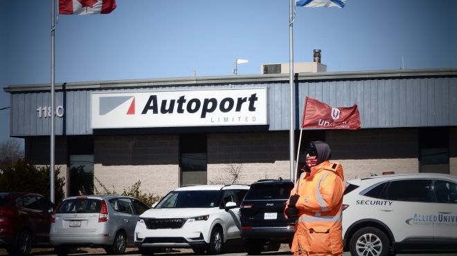 Unifor member waves a flag as they walk past CN Autoport office building