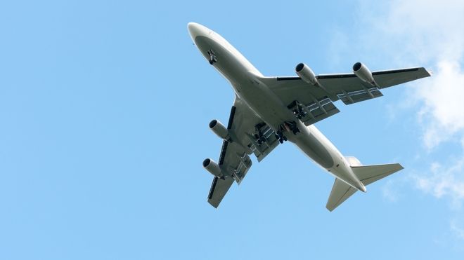 An airplane flying in a clear blue sky with little clouds.