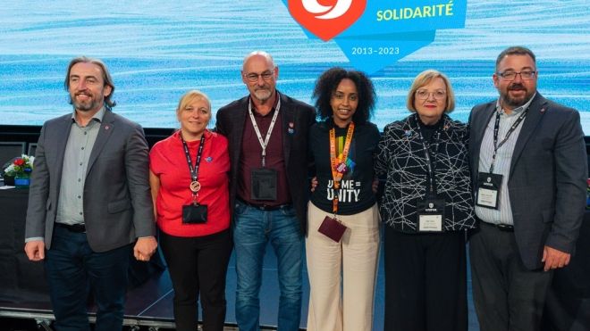 Three men and three women posing for a photo together in front of a video screen with a Unifor 10th anniversary logo.