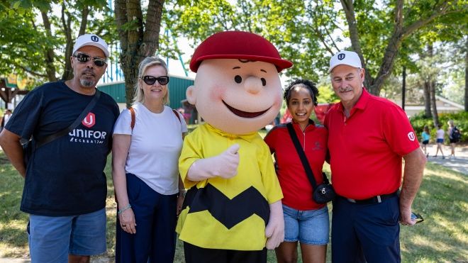 Four people pose with a peanuts character