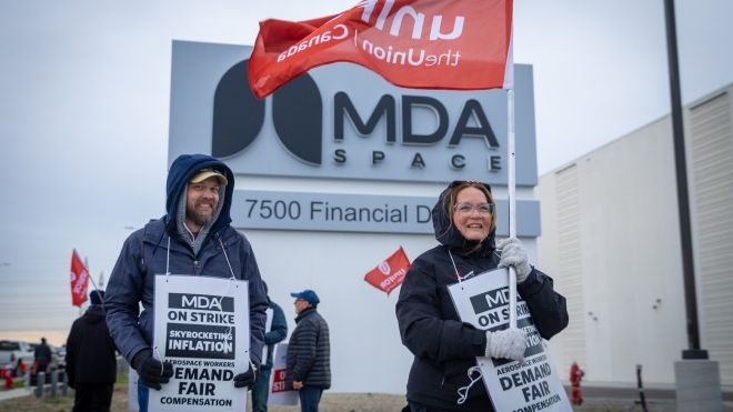 Aerospeace workers walking the picket line in front of the MDA Space headquarters in Brampton, Ontario holding picket signs and flags.