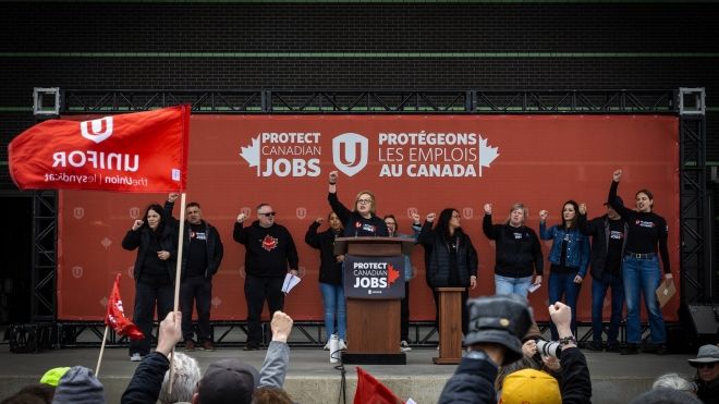 A woman shouts and raises her fist on stage with others, looking into a crowd.