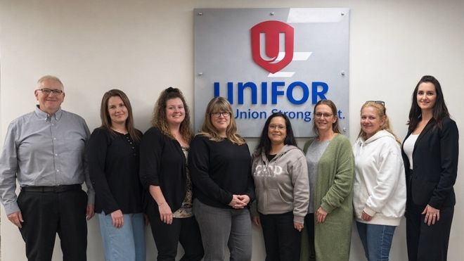 A group of eight standing in front of a Unifor sign