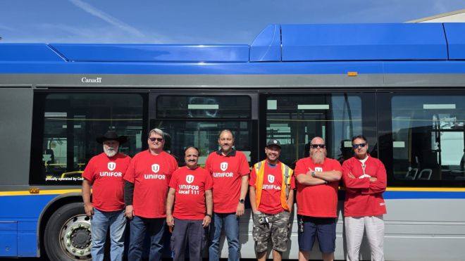A group of people wearing red Unifor t-shirts standing beside a Coast Mountain Bus