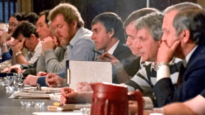 A group of men sitting at a table in a row, dence smoke fills the air.