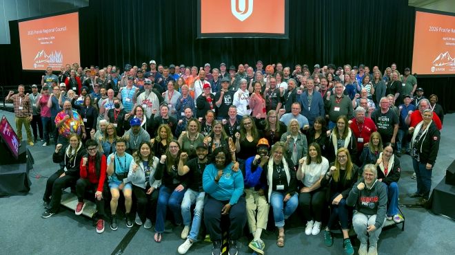More than one hundred delegates posing in front of a stage with Unifor logo on screens behind.