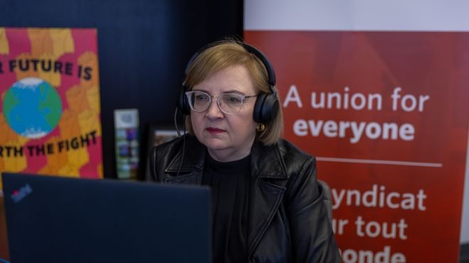 A woman wearing a headset sits at a computer screen.