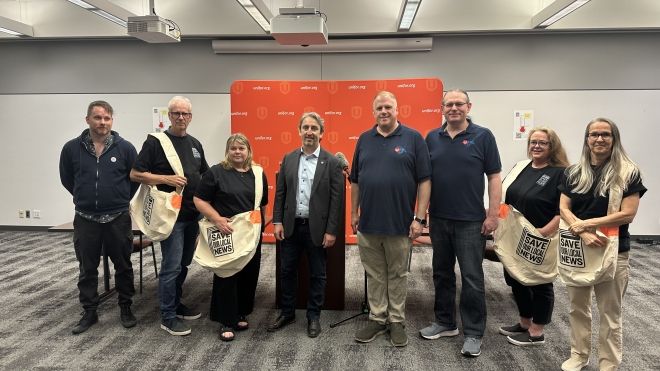 A group of people with Save Local News canvas bags standing in front of a red Unifor background.