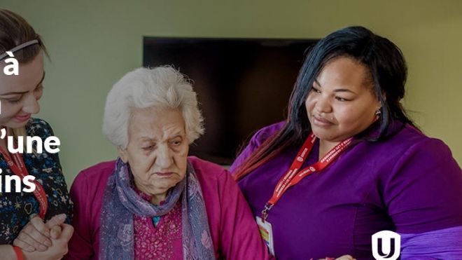 Une préposée aux services de soutien à la personne de race noire aide une personne âgée à se lever dans une maison de soins de longue durée