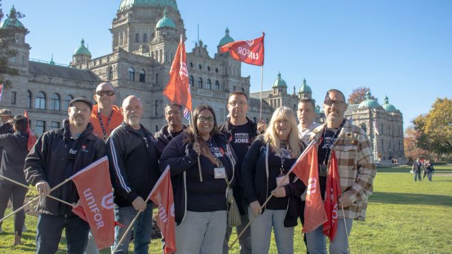 A group of Unifor members posing for a photo with flags. The B.C. legislature building is visible in the background.